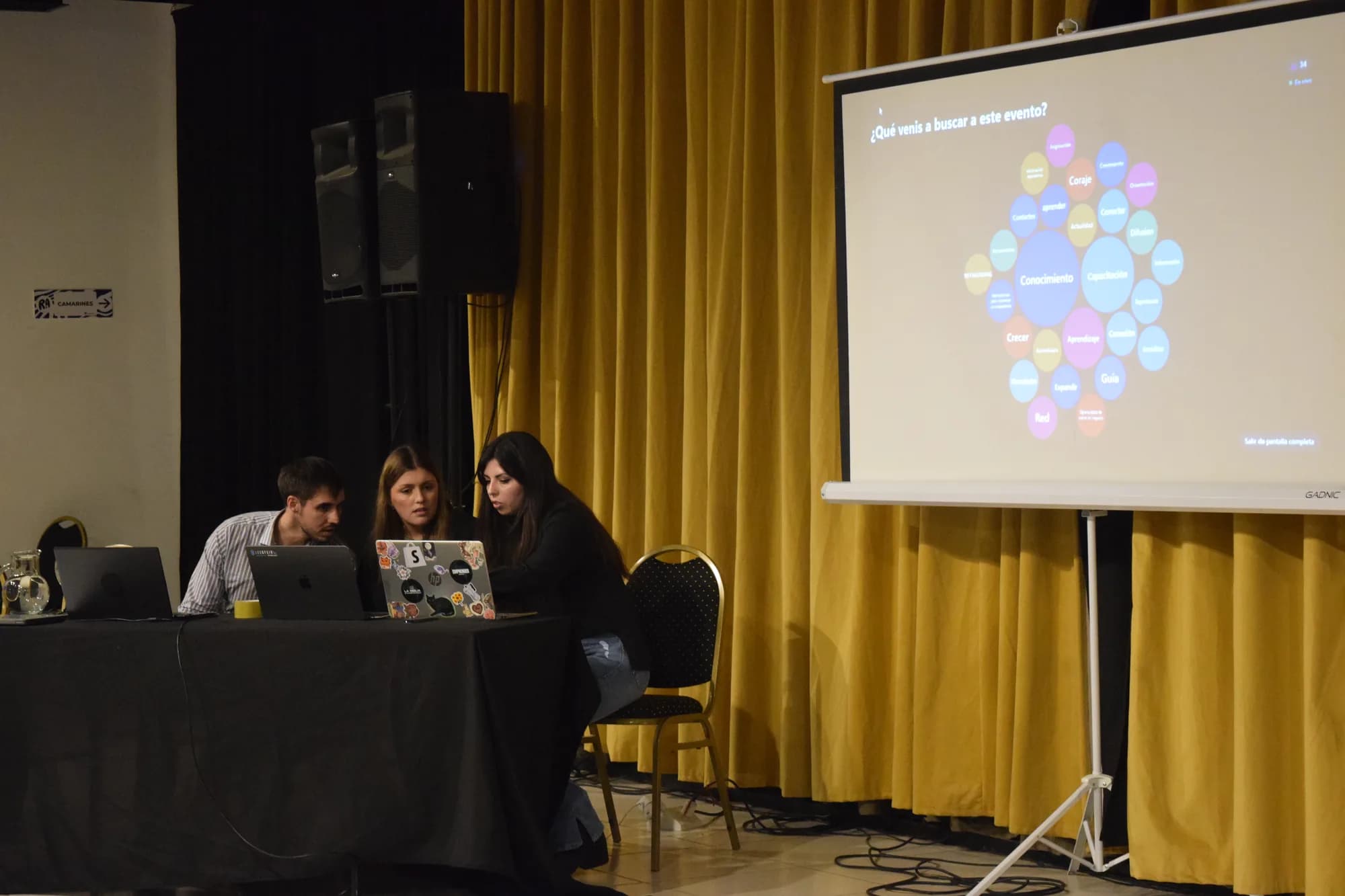 Mesa técnica junto al escenario, con la pantalla mostrando la primera consigna