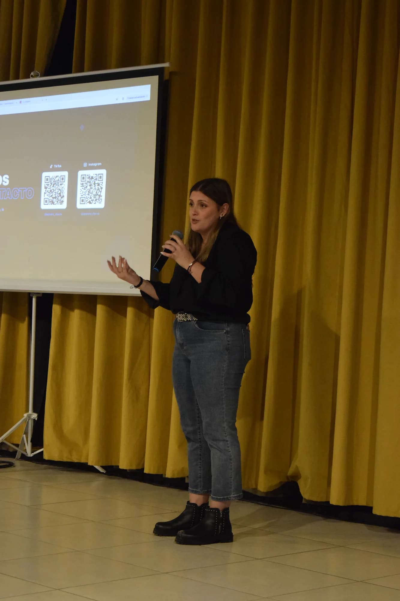Oradora habla con micrófono junto a una presentación con códigos QR