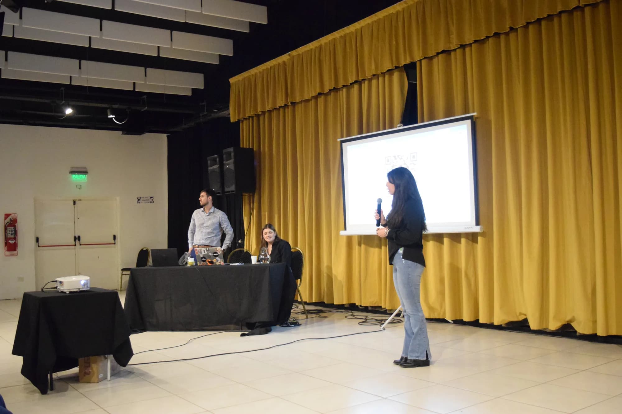 Presentadora habla frente a la pantalla con la mesa técnica detrás